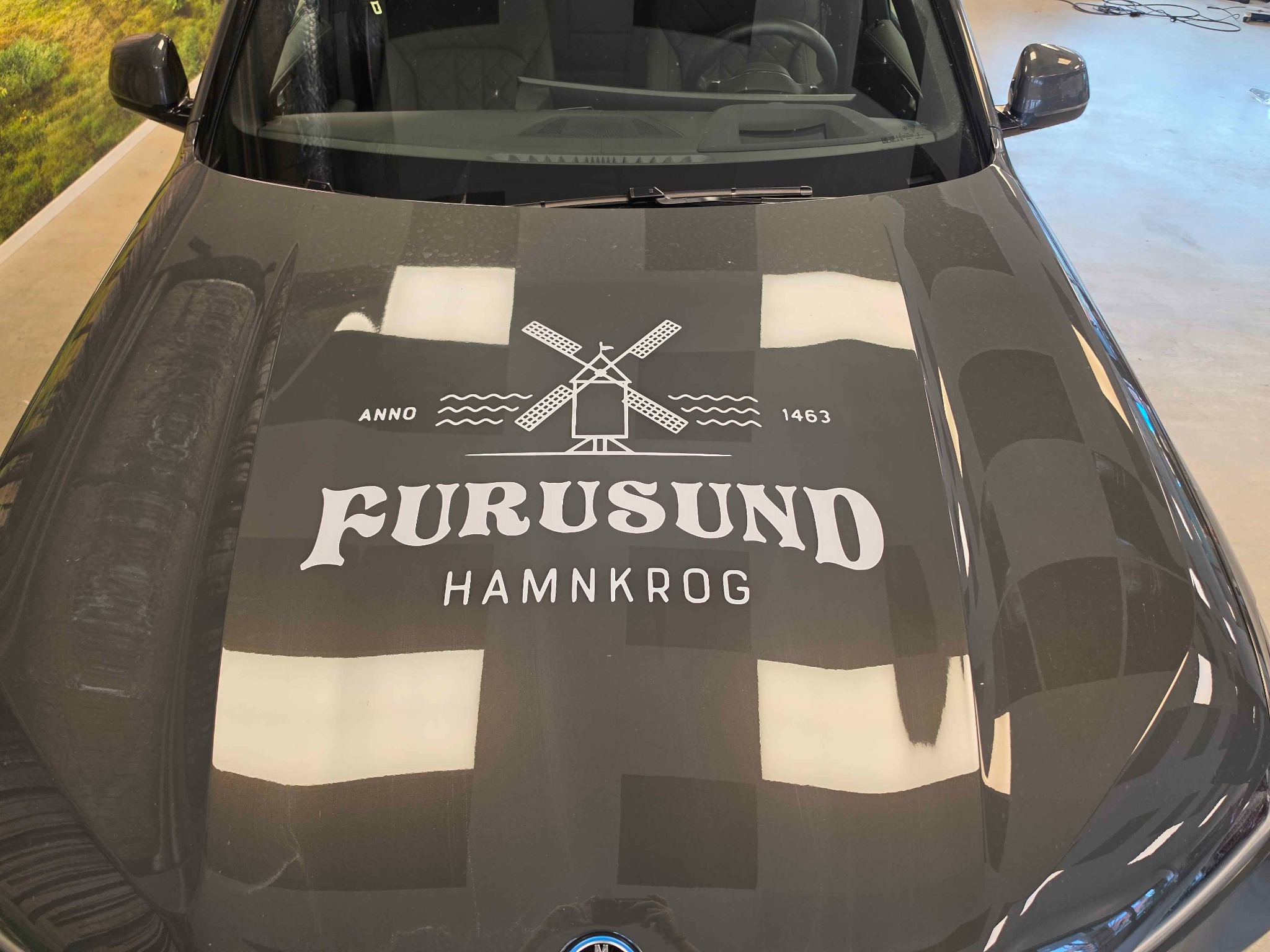 Vit utskuren logotyp för Furusund Hamnkrog monterad på motorhuven